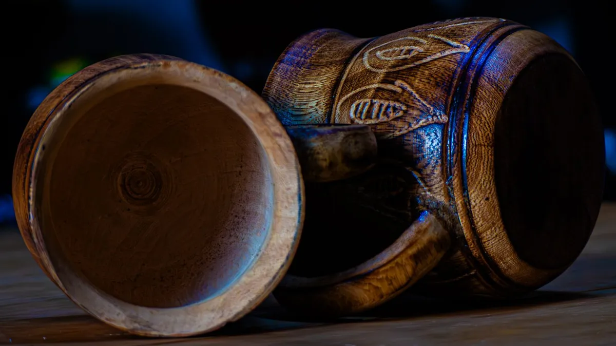 Two carved wooden drinking vessels rest on their sides in dark light.