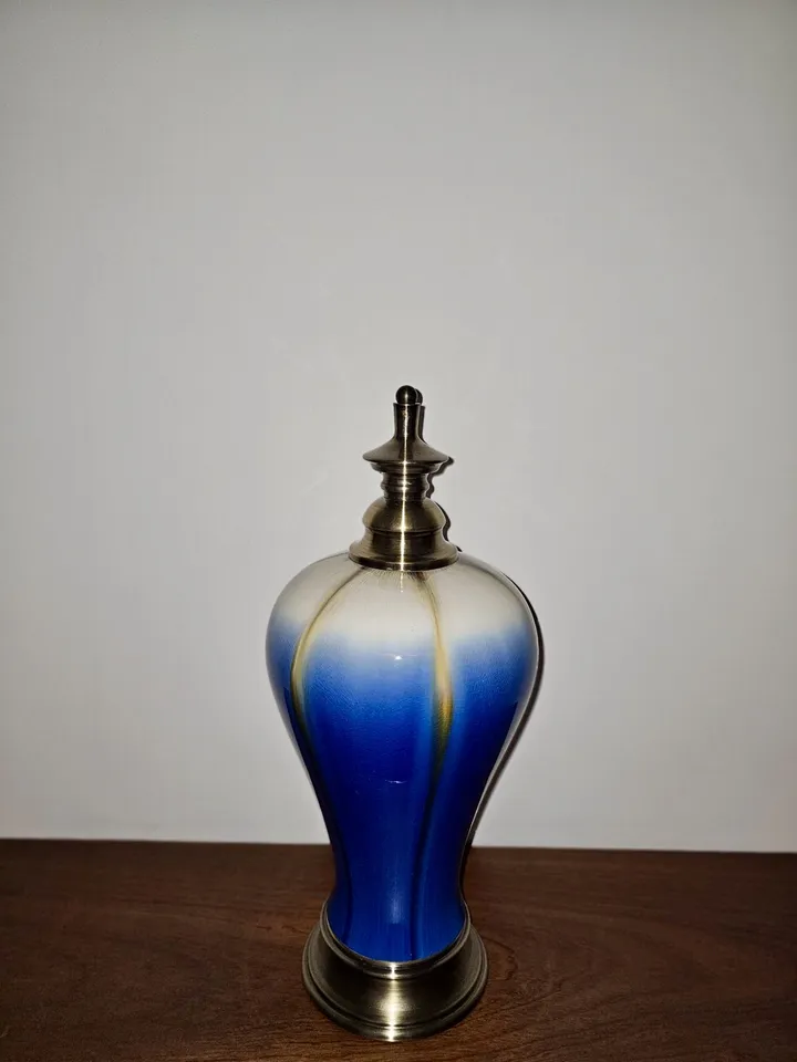 A blue-and-white decorative bottle with a metal lid stands on a wooden surface against a plain wall.