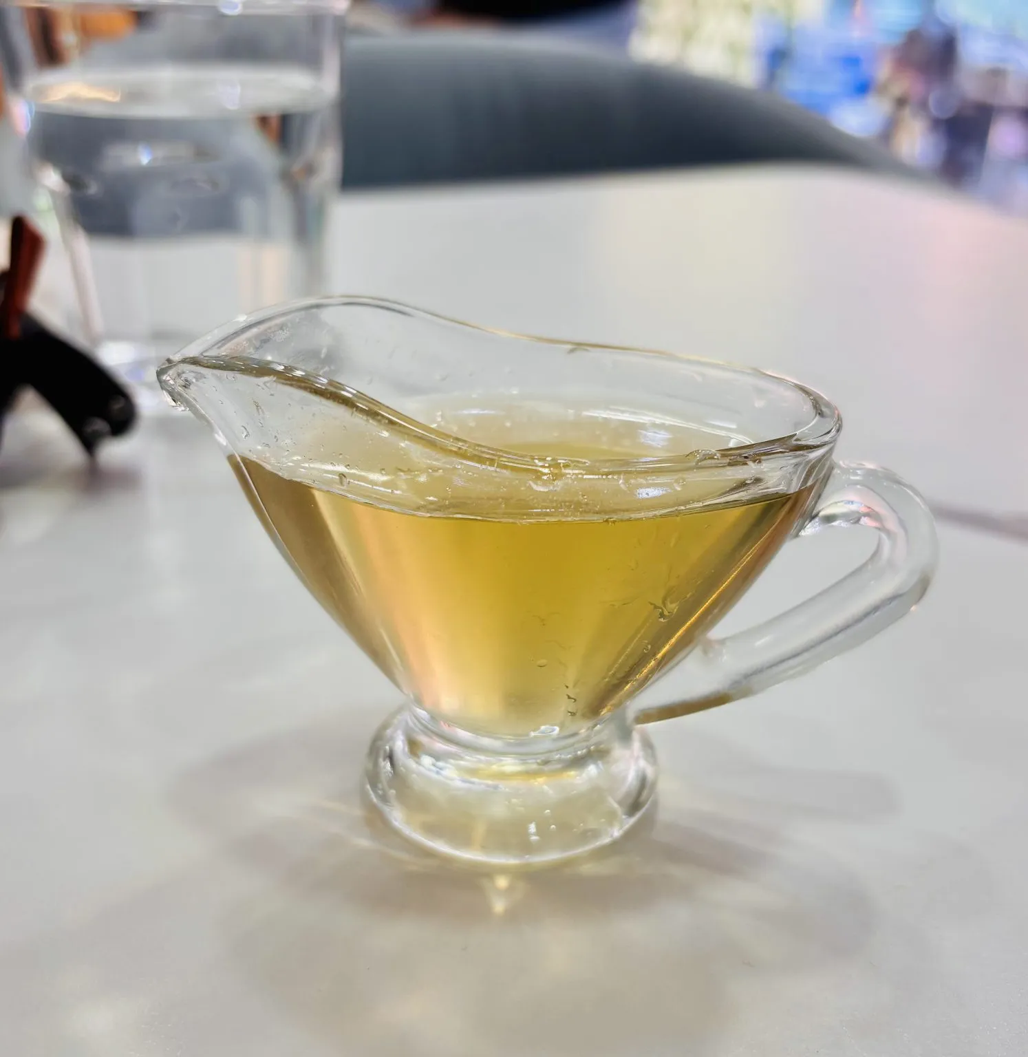 A small glass jug containing a pale golden liquid stands on a white tabletop.